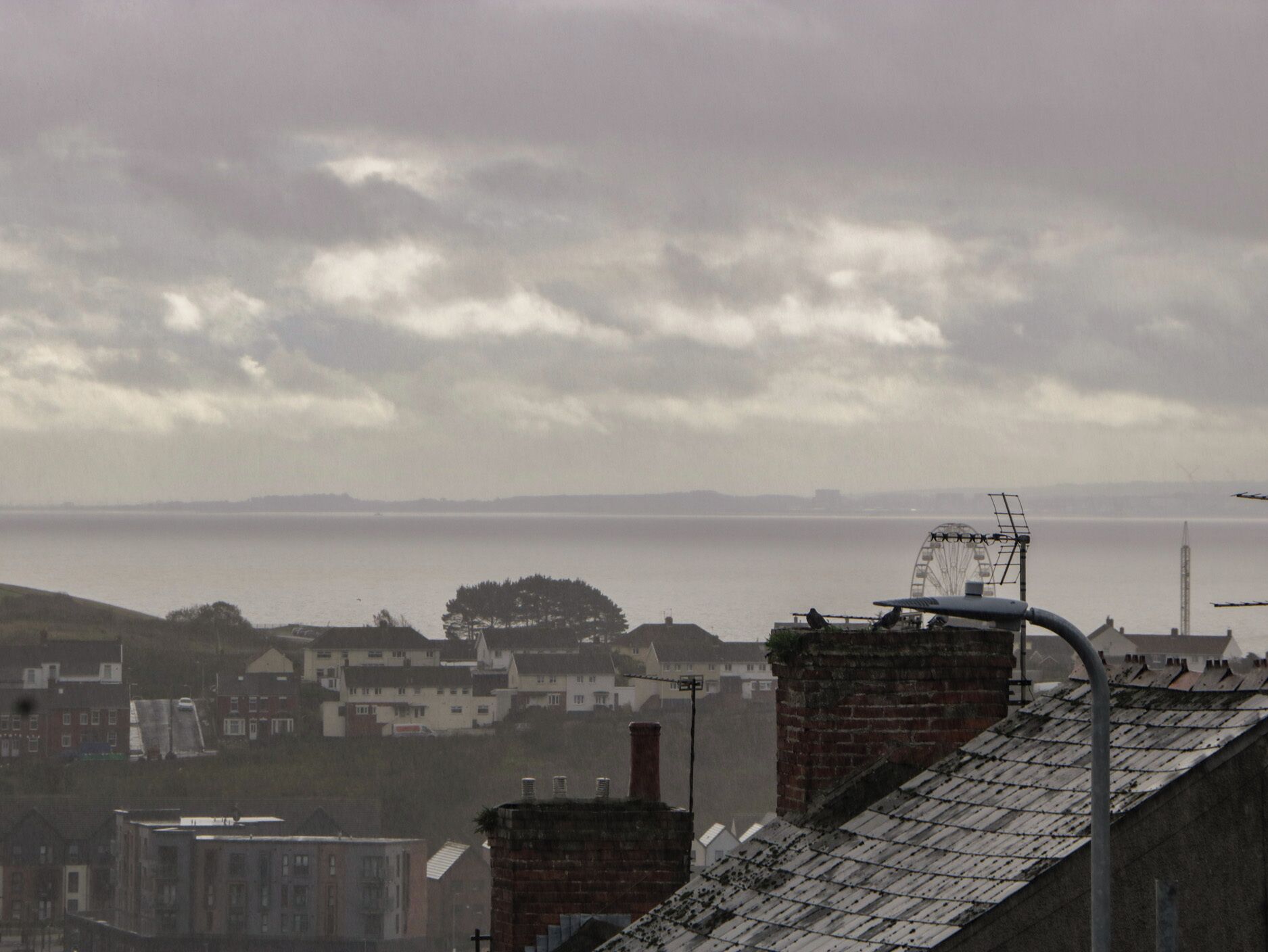 A residential area with houses, a hill, and a body of water in the distance.