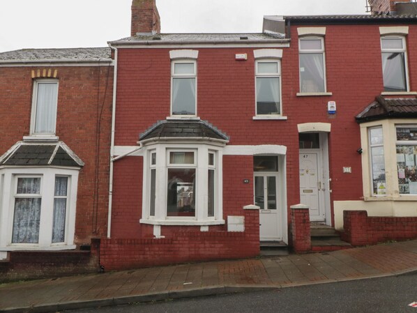 A red brick terraced house with a bay window, white door, and a small porch. - Lush House (Barry)