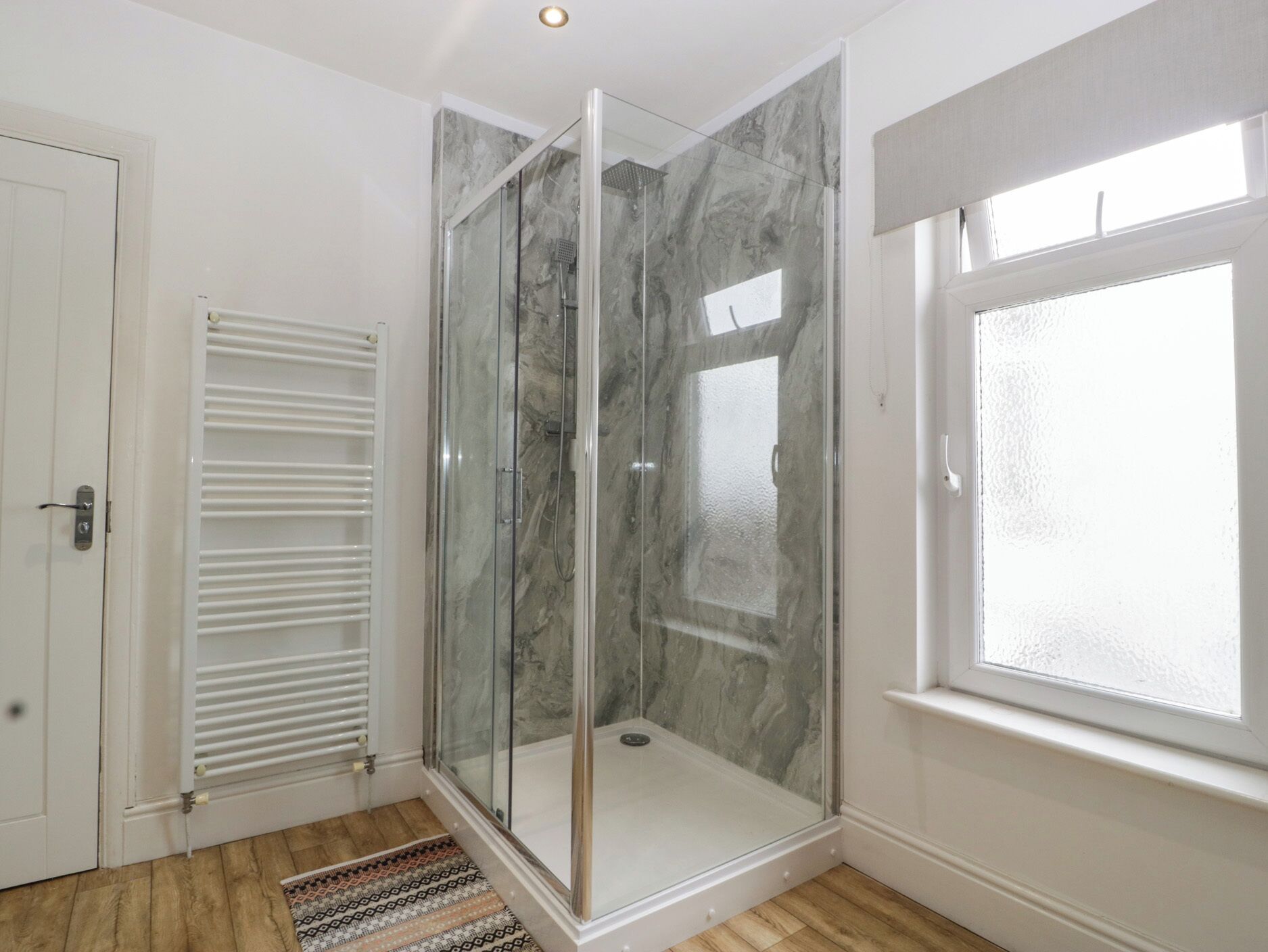 A modern bathroom with a glass-enclosed shower, a white door, and a window.