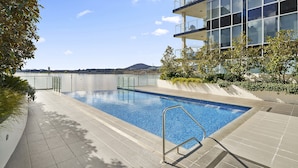 A swimming pool with a clear view of the sky and distant landscape, surrounded by modern architecture and greenery. - Stylish 1-bed Retreat Steps From Foreshore (Canberra)