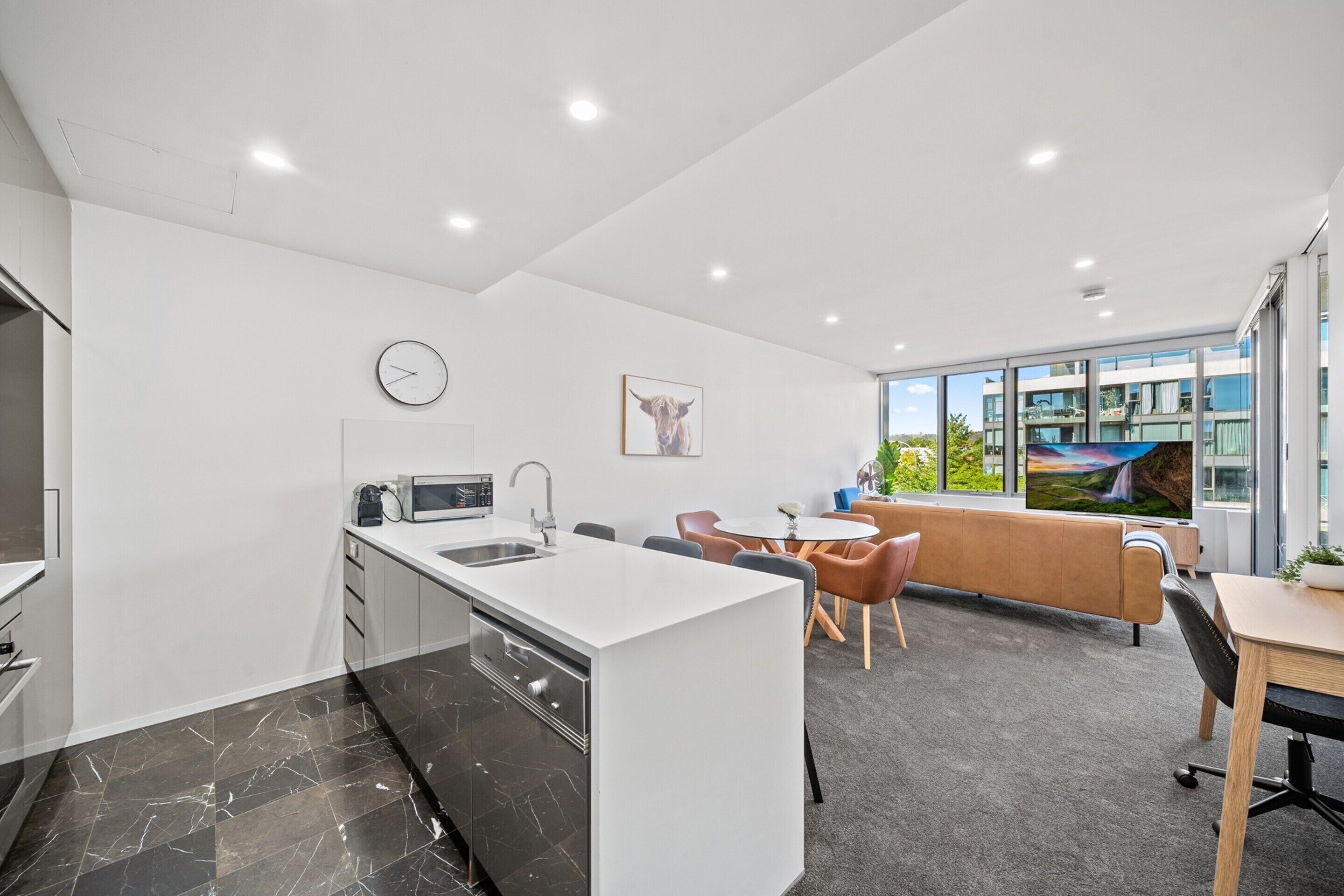 Een moderne keuken met een wit kookeiland, een eethoek met een ronde tafel en stoelen, en een groot raam met uitzicht.
