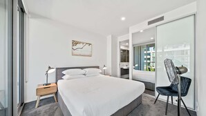 A modern hotel room with a large bed, a bedside table with a lamp, a chair, a large window, and a view of the city. - Stylish 1-bed Retreat Steps From Foreshore (Canberra)