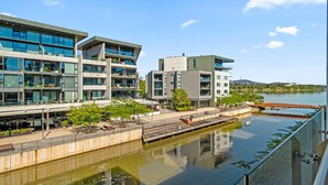A modern building with multiple floors, large windows, and a waterfront view. - Stylish 1-bed Retreat Steps From Foreshore (Canberra)