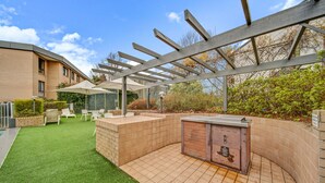 Un espacio patio con césped artificial, una parrilla, mobiliario exterior y una estructura pérgola.