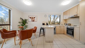 Una cocina moderna con una isla central, armarios de madera y un comedor con sillas naranjas.