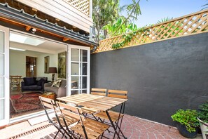 An outdoor patio with a wooden table and chairs, a red patterned rug, and a view of the interior through a glass door. - Stylish Inner-city Terrace Home With Rooftop Deck (Sydney)