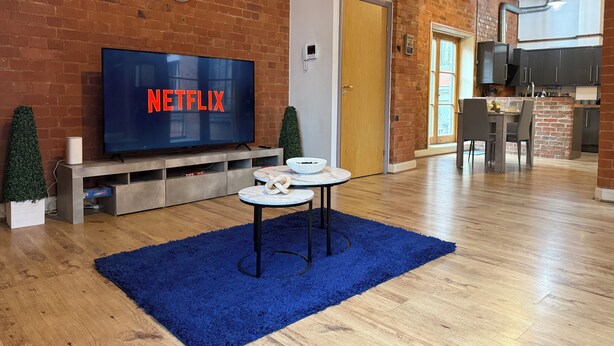 A modern living room with a brick wall, a flat-screen TV displaying 'NETFLIX', a small round table, and a blue rug.