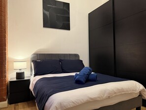 Ein Schlafzimmer mit einem Bett, einem Nachttisch, einer Lampe und einem Wandbild.