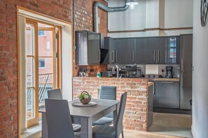 A modern kitchen with a brick wall, a dining area with a table and chairs, and a view through an open door.