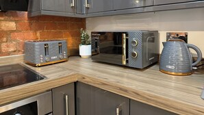 A kitchen with grey cabinets, a toaster, a microwave, and a kettle on a wooden countertop.