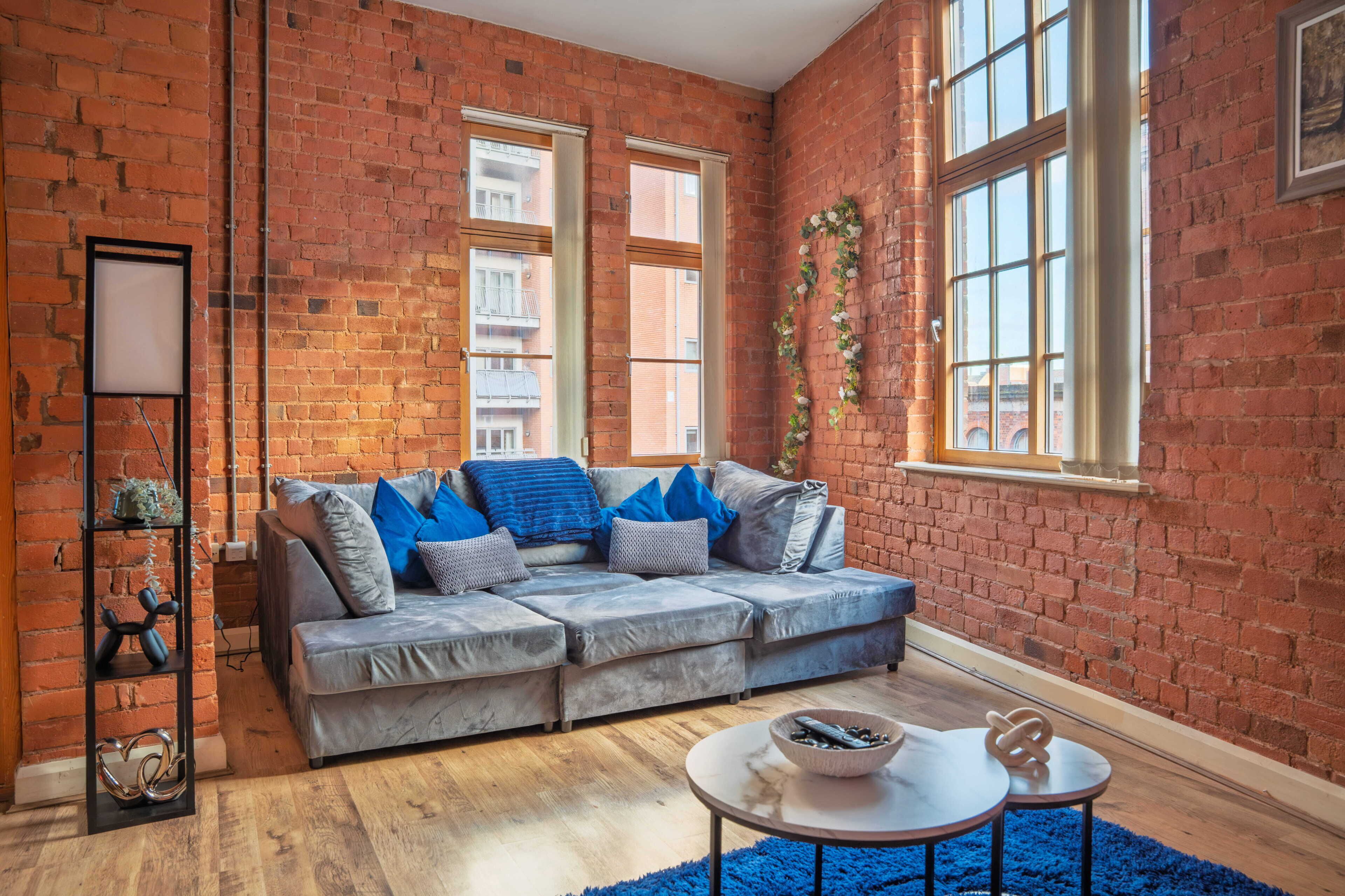 A cozy living room with a grey sofa, a blue rug, and a brick wall.