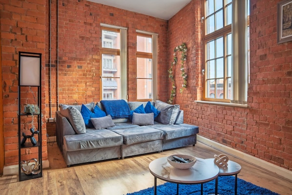 A cozy living room with a grey sofa, a blue rug, and a brick wall.