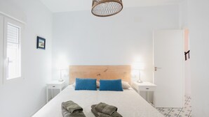 Ein ordentlich eingerichtetes Hotelzimmer mit einem großen Bett, zwei Nachttischen mit Lampen, einem hölzernen Kopfteil und einer Tür mit schwarzem Griff.
