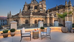 A historic building with a clock tower, outdoor seating with chairs and tables, and potted plants.