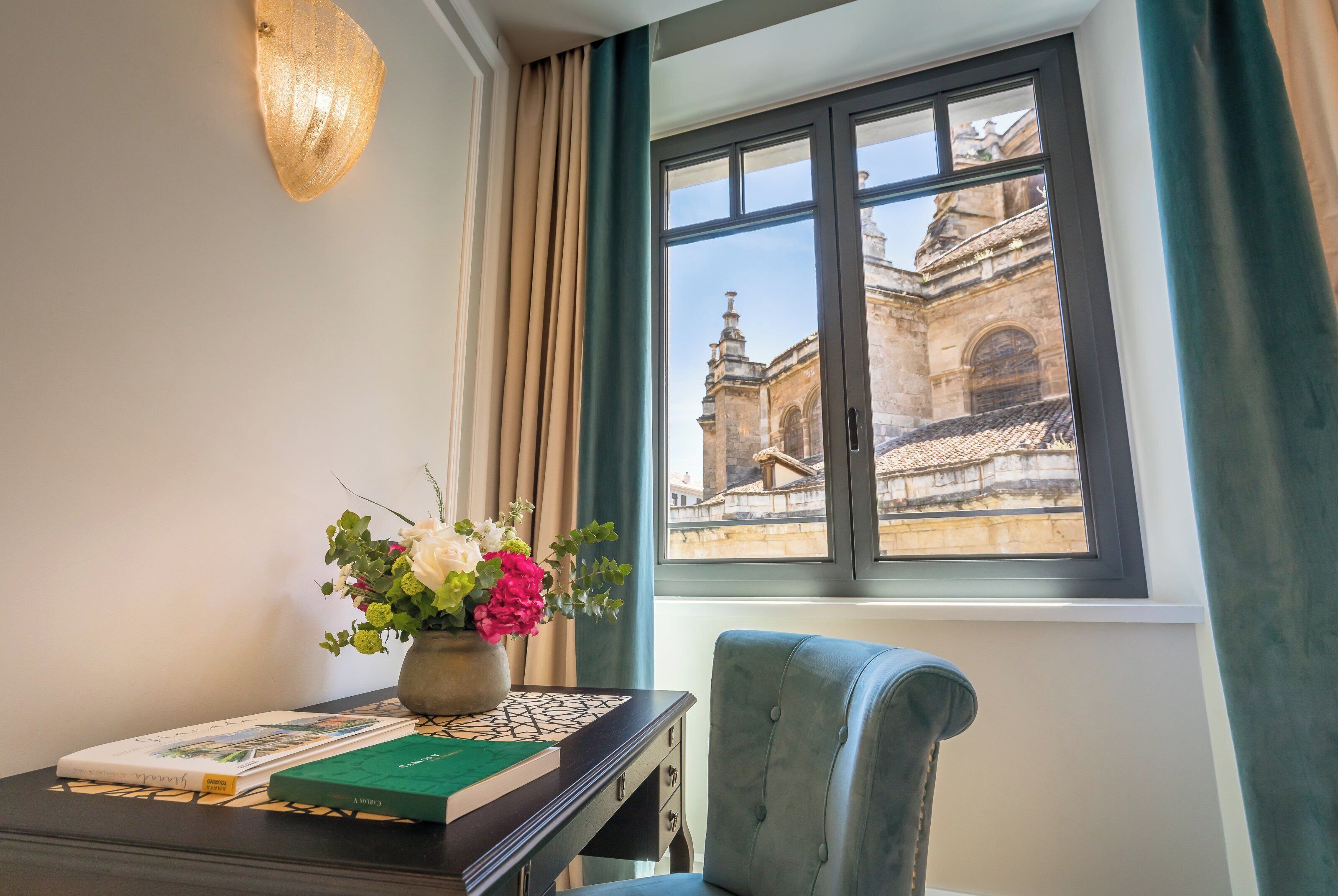 A room with a desk, a vase of flowers, and a window with a view of a historic building.