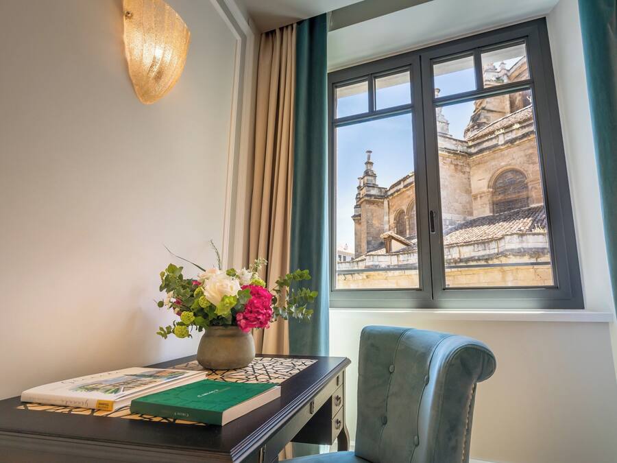 A room with a desk, a vase of flowers, and a window with a view of a historic building.