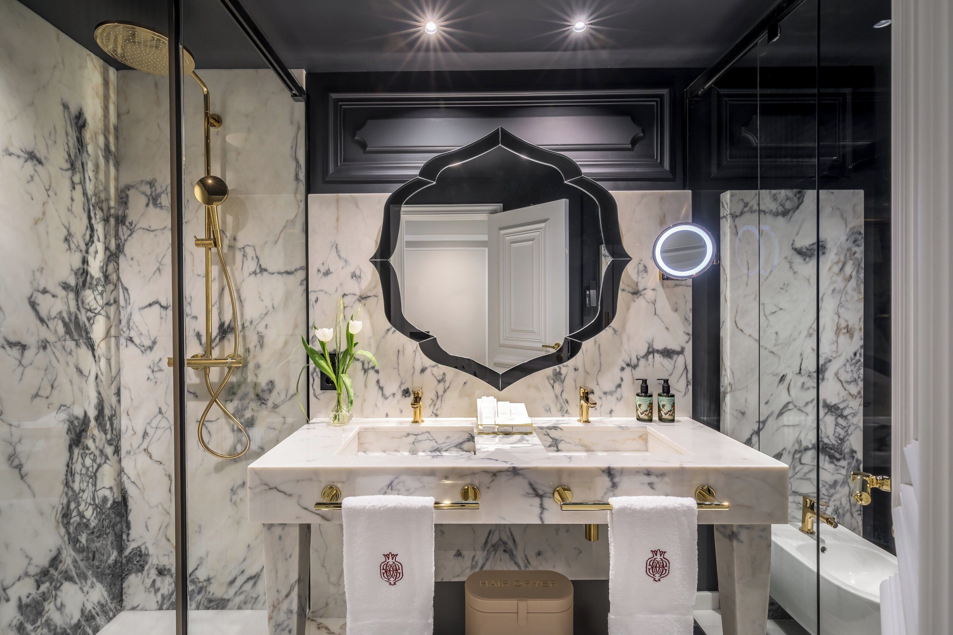 Un bany modern amb un lavabo de marbre, accessoris daurats, un mirall gran i una banyera.