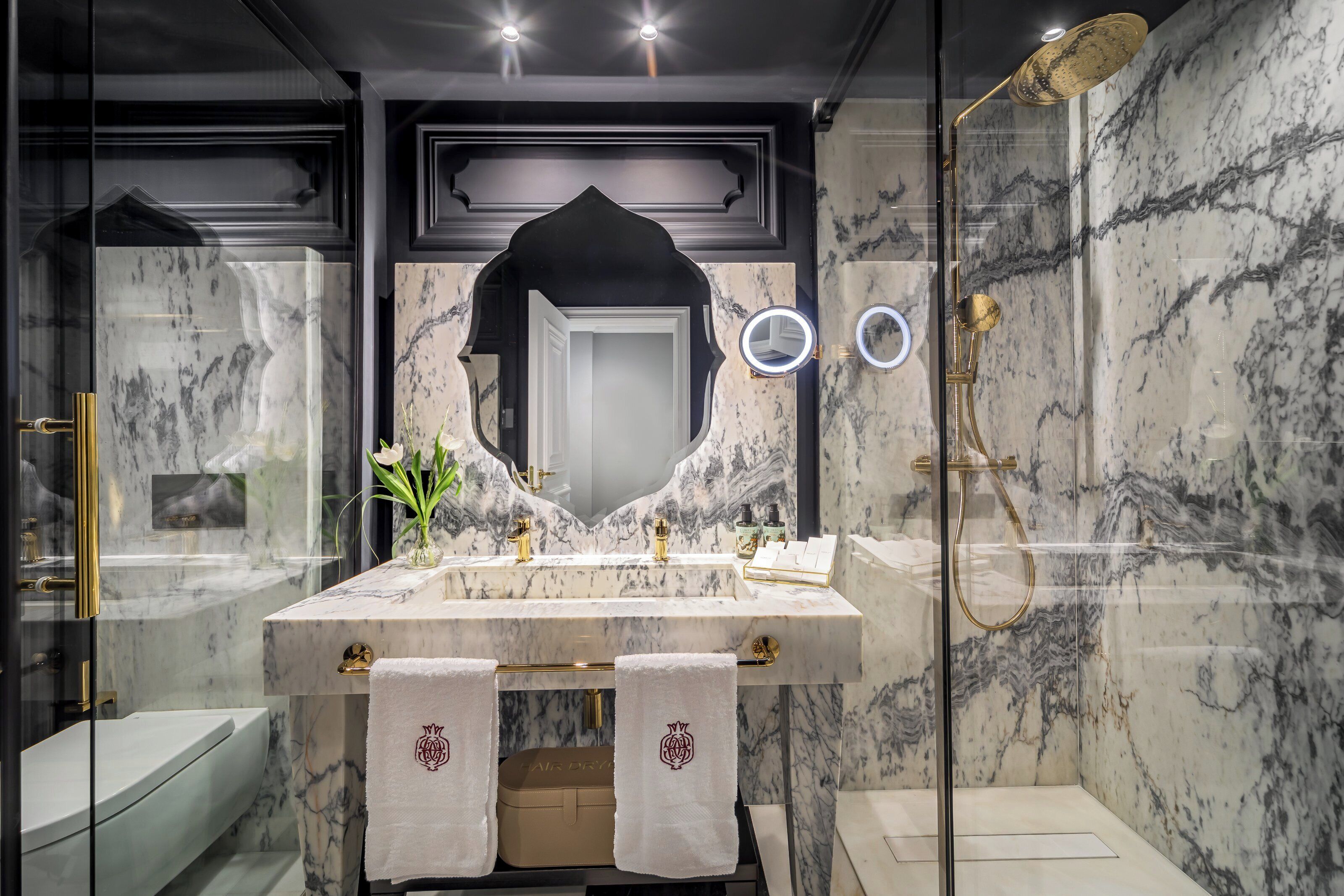 A modern bathroom with a marble vanity, a glass-enclosed shower, and a large mirror with a decorative frame.