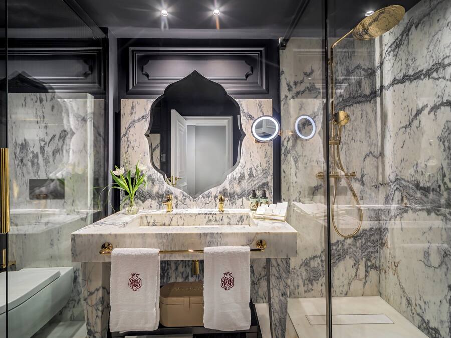 A modern bathroom with a marble vanity, a glass-enclosed shower, and a large mirror with a decorative frame.