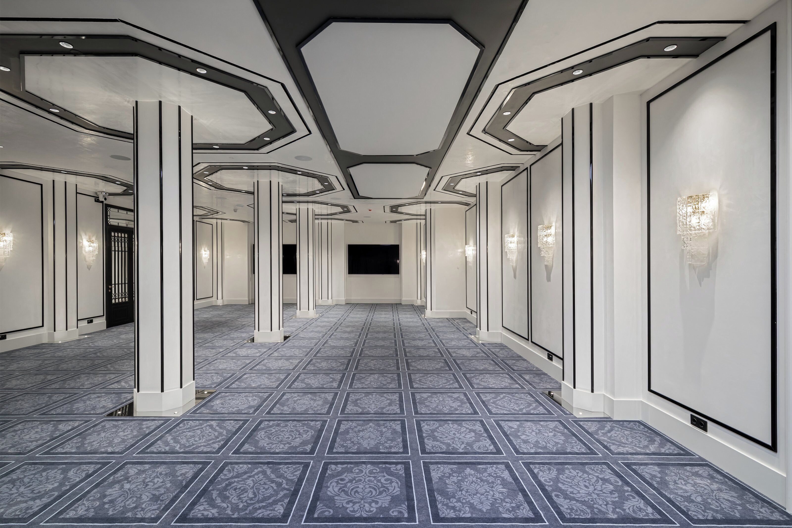 Un pasillo con suelo estampado, paredes blancas y columnas.