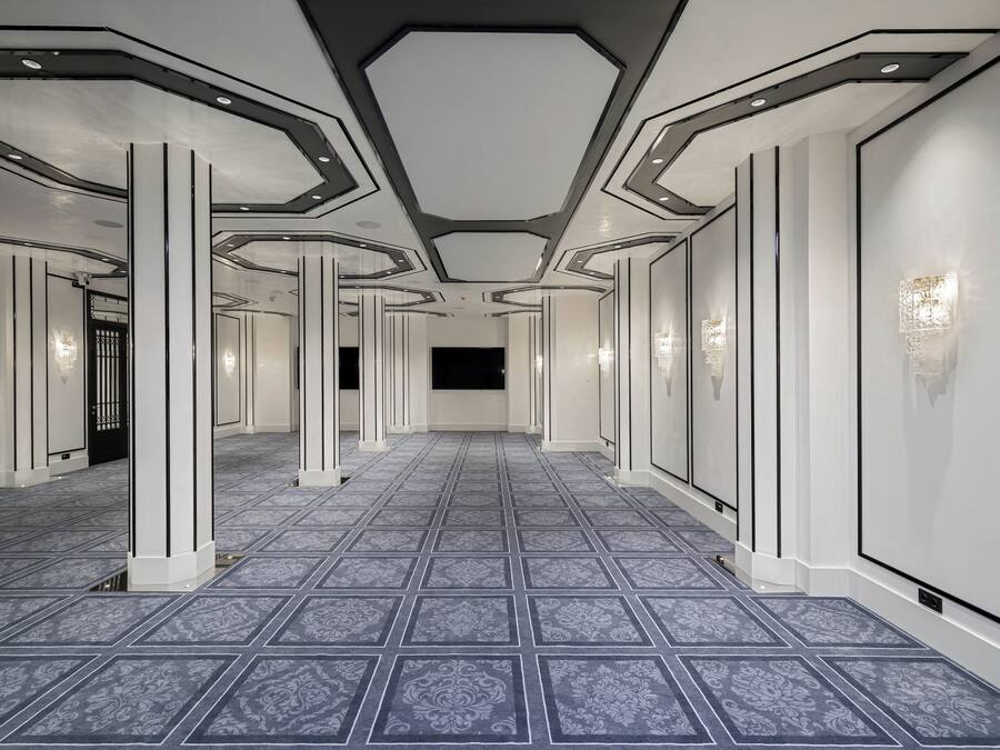 Un pasillo con suelo estampado, paredes blancas y columnas.