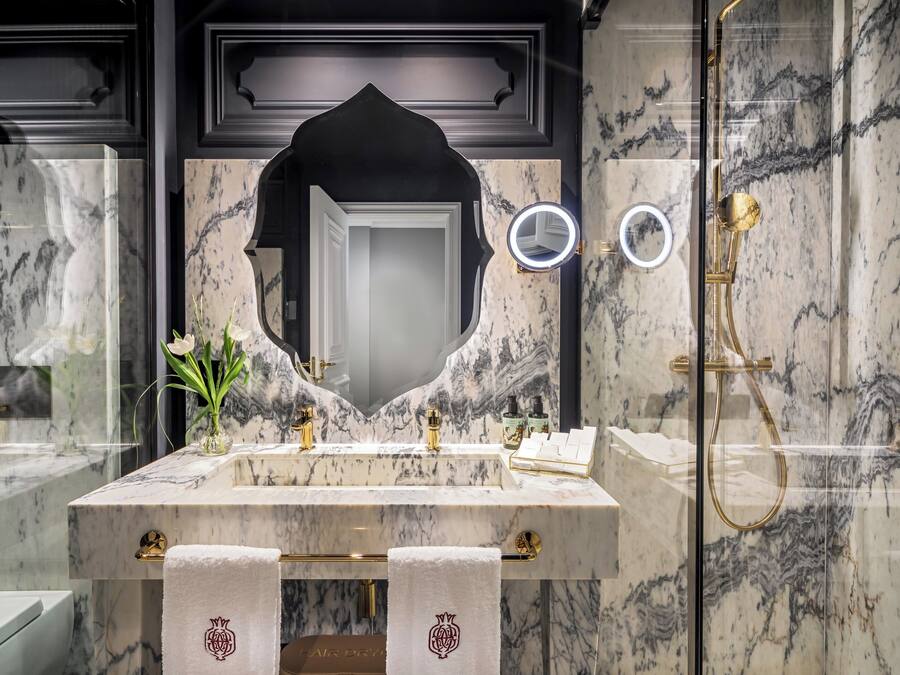 Une salle de bain en marbre avec un grand miroir, des accessoires dorés et une pomme de douche dorée.