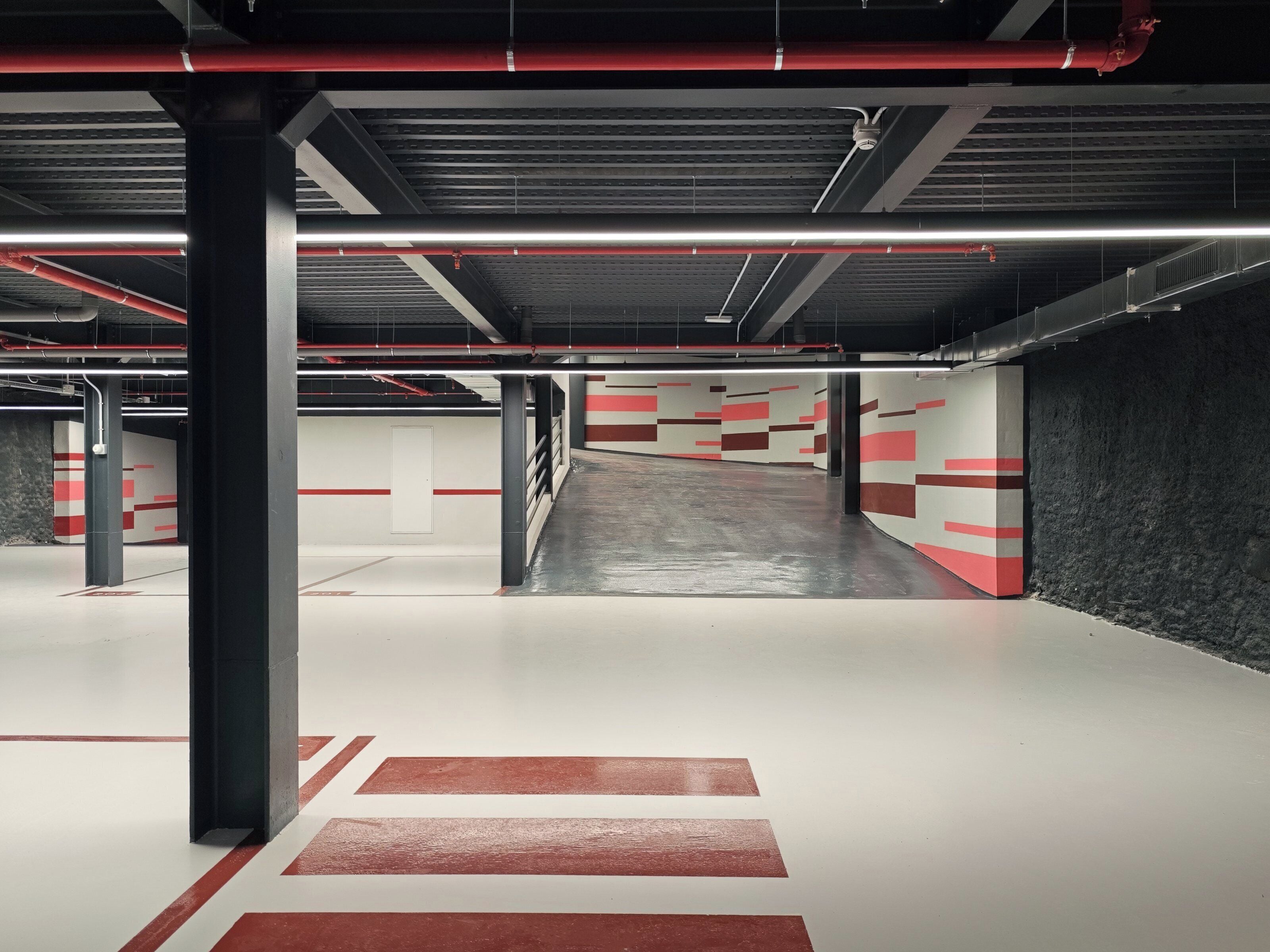 A multi-level parking garage with red and white striped walls, metal pillars, and overhead lighting.