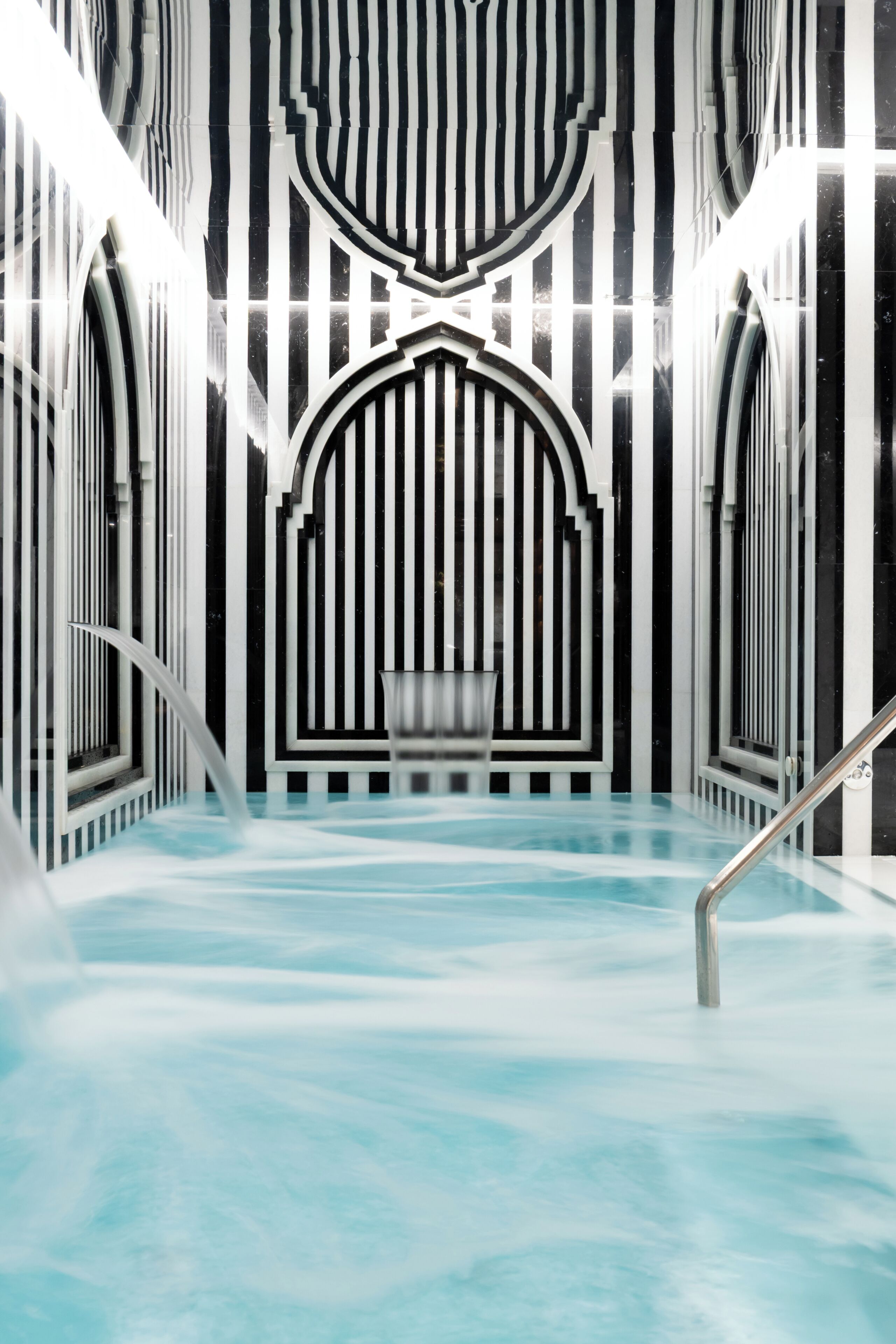 Piscina interior moderna con diseños geométricos en las paredes y una fuente central.
