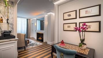 Quarto de hotel com lareira, área de jantar com mesa e cadeiras, e parede com quadros emoldurados.