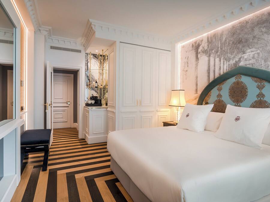 A hotel room with a large bed, a bench, a desk, and a mirror.