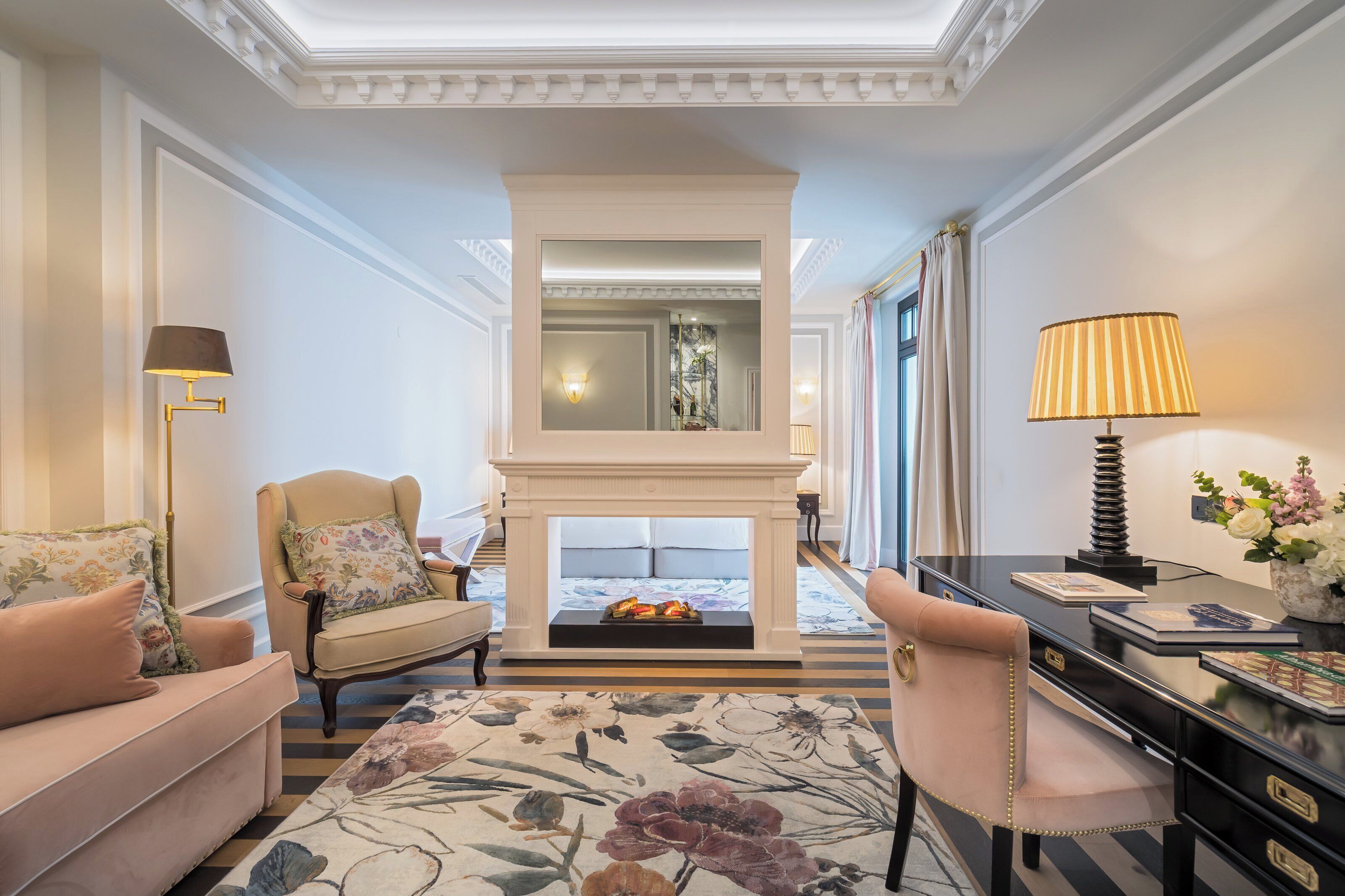 A room with a fireplace, a sofa, a chair, a desk, and a lamp.