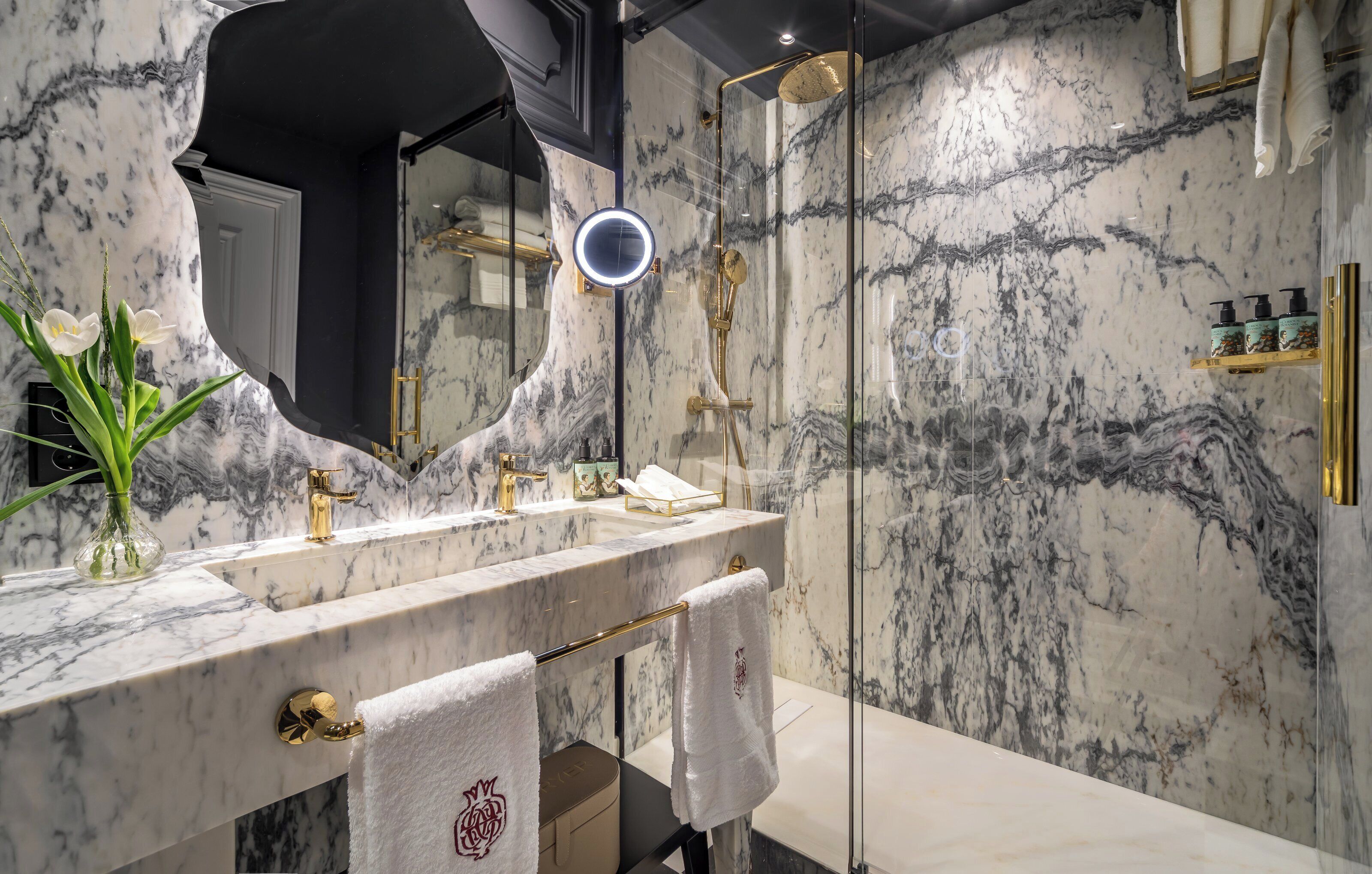 A bathroom with a marble vanity, a glass shower enclosure, and a round mirror.