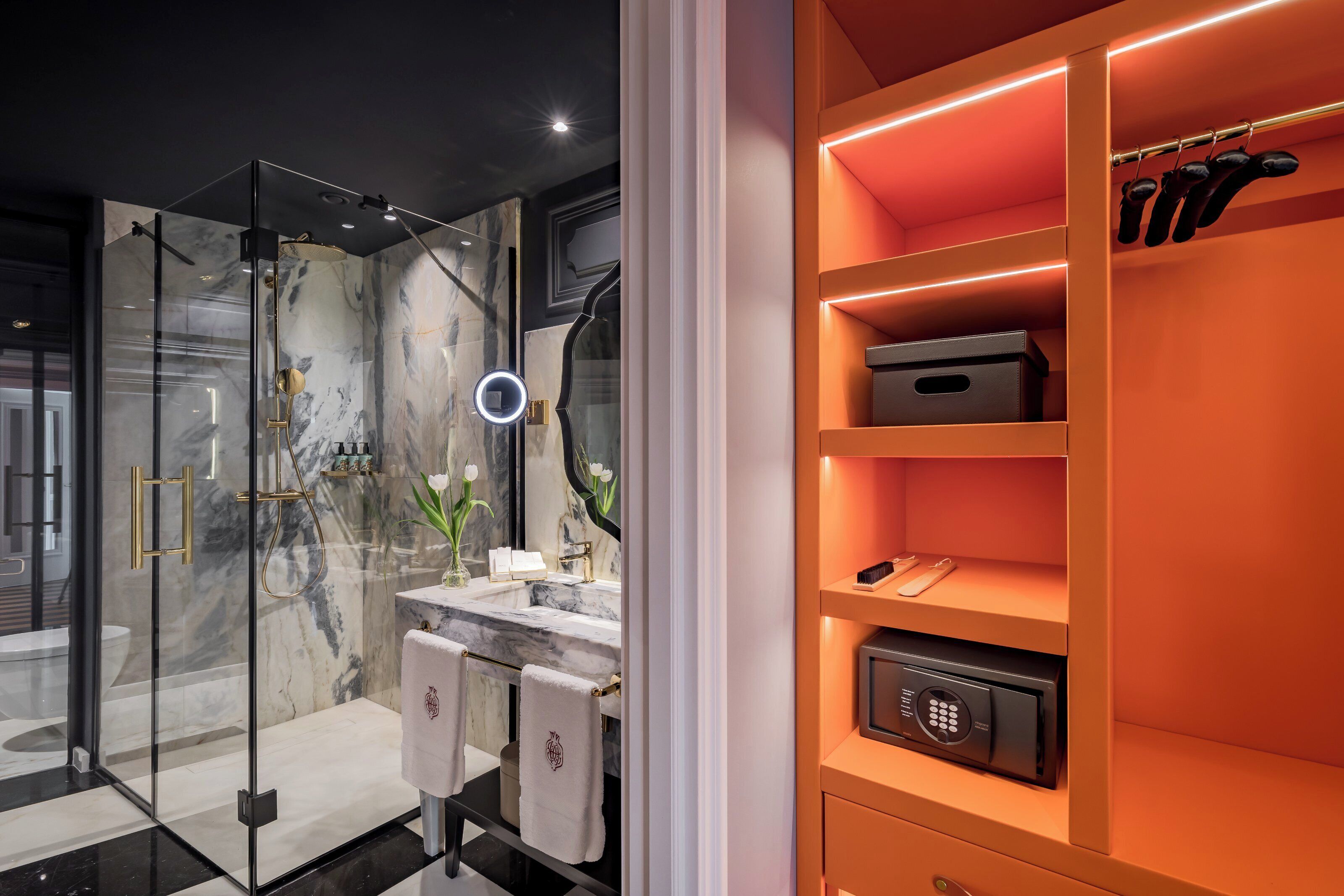 Une salle de bain moderne dotée d’une douche à parois de verre, de murs en marbre, d’un meuble-lavabo avec miroir et d’un coffre-fort encastré.