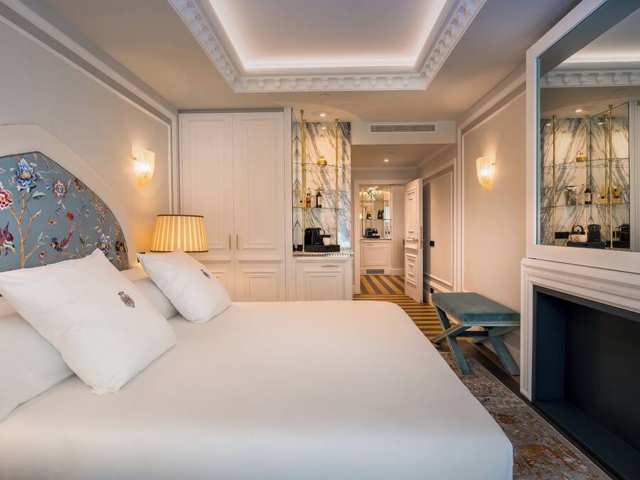 A hotel room with a large bed, a small table, a mirror, and a fireplace.