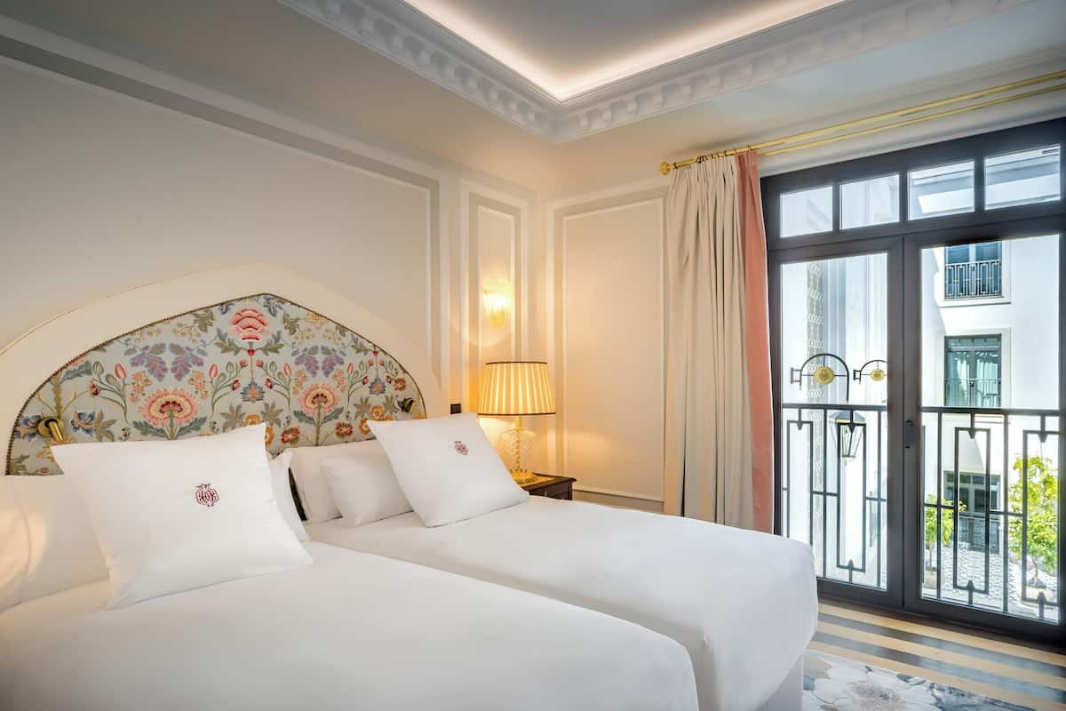 A hotel room with a large bed, a nightstand, a lamp, and a view of the outside balcony.