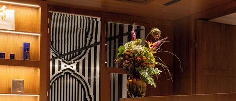 A reception area with a wooden reception desk, a vase with flowers, and a black and white striped wall.