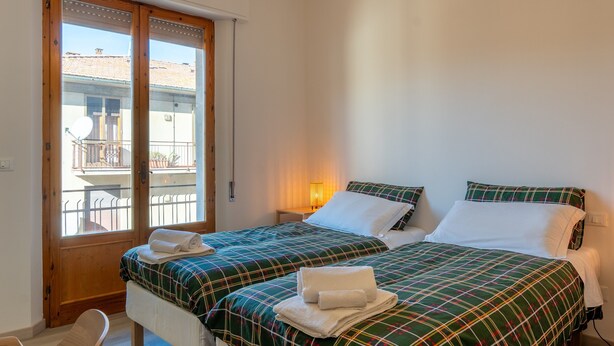 A bedroom with two beds, a wooden door, a balcony, and a nightstand with a lamp. - Room in the Heart of Val d'Orcia with Balcony and Wi-Fi (Montepulciano)