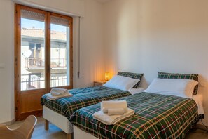 Un dormitorio con dos camas, una puerta de madera, un balcón y una mesita de noche con lámpara.