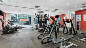 Une salle de sport équipée de divers appareils d’exercice, d’un tapis de course et d’un mur recouvert de miroirs.