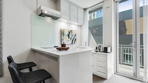 Une cuisine moderne avec un plan de travail blanc, une machine à café et une vue sur l’extérieur.