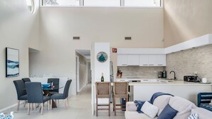 A modern living room with a sofa, dining table, and chairs. There is a kitchen area with a sink, stove, and cabinets. - 3-bed With Beach Views and Entertainment Area (Denhams Beach)