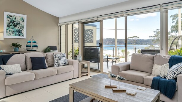 A modern living room with two sofas, a coffee table, and a view of the sea through large glass doors. - 3-bed With Beach Views and Entertainment Area (Denhams Beach)