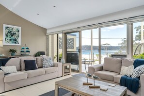 A modern living room with two sofas, a coffee table, and a view of the sea through large glass doors. - 3-bed With Beach Views and Entertainment Area (Denhams Beach)