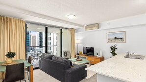 Een moderne hotelkamer met een zithoek, kitchenette en een groot raam met gordijnen.