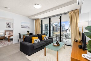 A modern living room with a sofa, coffee table, and a view of the city through large windows. - 1-bed Brisbane Apt With Pool & Gym (Brisbane)