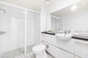 Een moderne badkamer met een douchecabine van glas, een wit wastafelmeubel en een toilet.