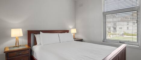 A neatly made bed with white linens, a wooden headboard, and two bedside lamps.