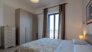 A bedroom with a bed, a dresser, a window with curtains, and a wall-mounted lamp. - Terrazza sul mare (Santa Maria di Castellabate)
