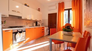 A modern kitchen with orange cabinets, a dining table with orange chairs, and a window with orange curtains. - Terrazza sul mare (Santa Maria di Castellabate)