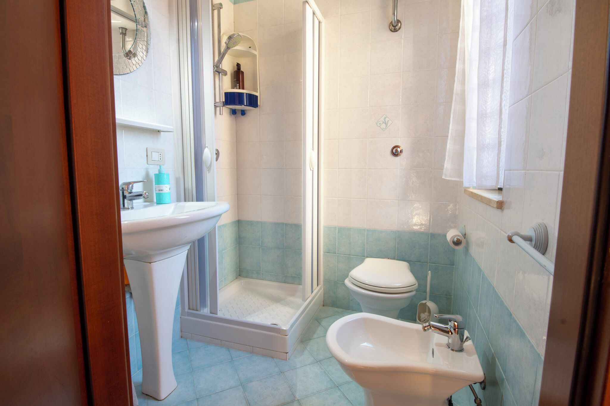 Baño con ducha, inodoro, lavamanos y espejo.